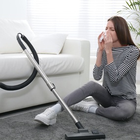 Young lady experiencing an allergic reaction from vacuuming the living room. Concept, Flotex Flooring doesn’t cause allergic reactions.