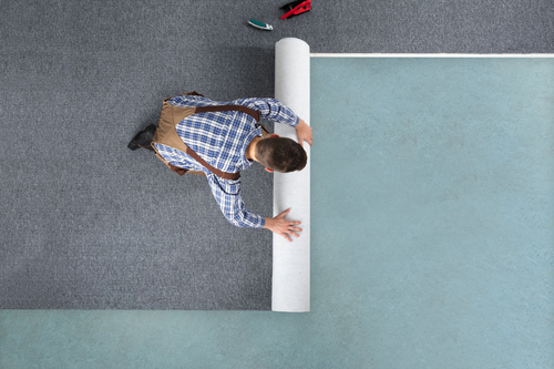 A professional carpet installer is rolling out Flotex carpeting on the floor in this high-angle shot.