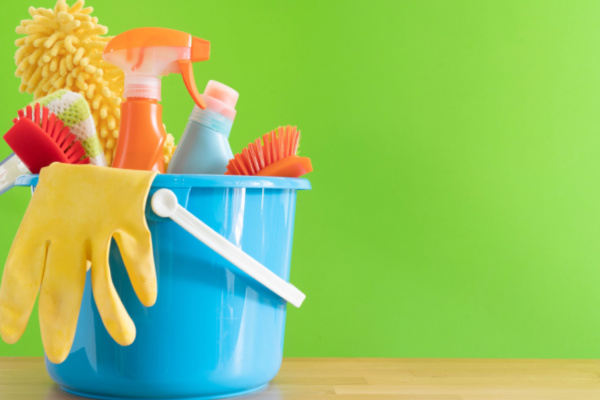 A wood table equipped with carpet cleaning products in a blue bucket set against a green background. How to prepare for a carpet cleaning concept.