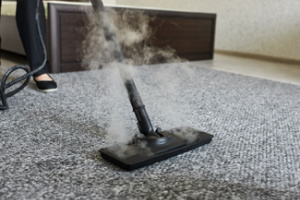 A close-up view shows a person using a steam cleaner to remove dirt from the carpet in their home. Concept, deep clean your carpets.