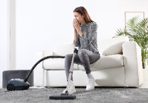 A young woman struggles with a dust allergy as she vacuums her home. The concept is carpet cleaning for allergy sufferers.