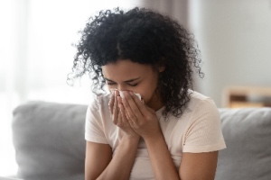 An allergic woman sneezes into tissue on the sofa, highlighting the need for carpet cleaning. The concept is carpet cleaning for allergy sufferers.