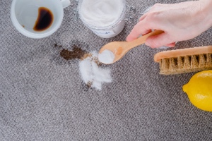 A person uses baking soda to clean a coffee stain on the carpet. The concept represents eco-friendly carpet cleaning solutions.