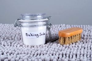 A wooden brush and baking soda on a gray carpet represent eco-friendly carpet cleaning solutions.